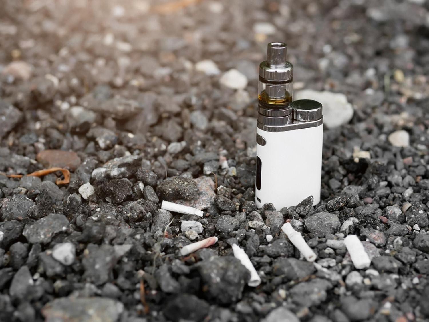 A compact white vape device on gravel with discarded cigarette butts, showing the shift in the UAE nicotine market